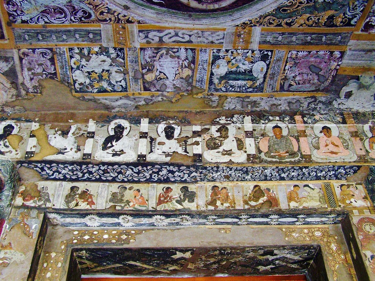 The ceiling is covered in decorative patterns, below is a row of Buddhas, and just above the doorway a couple of every day life scenes (cave 17)