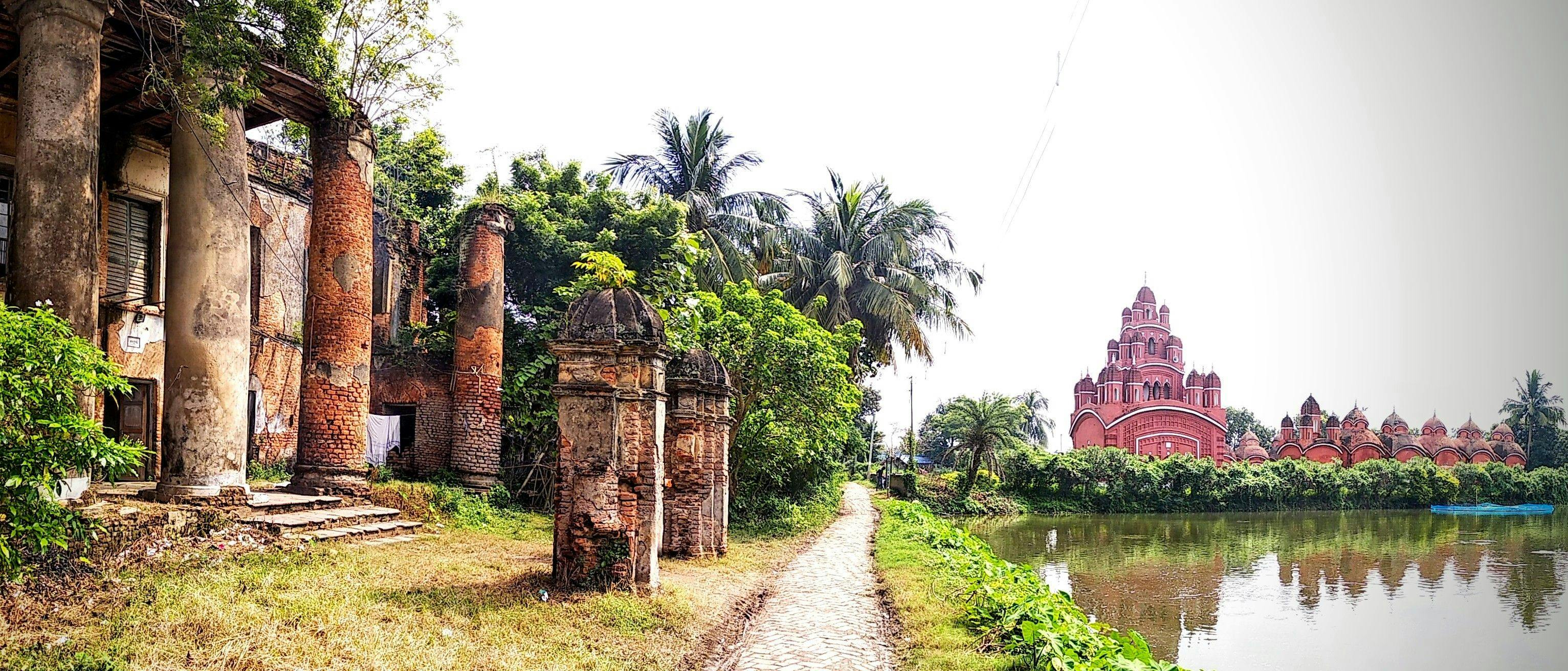 The huge columns of the Mustafi family mansion, Radha Kunja, and Ananda Bhairavi Temple complex on the banks of an adjacent water body in Sukharia-Somra