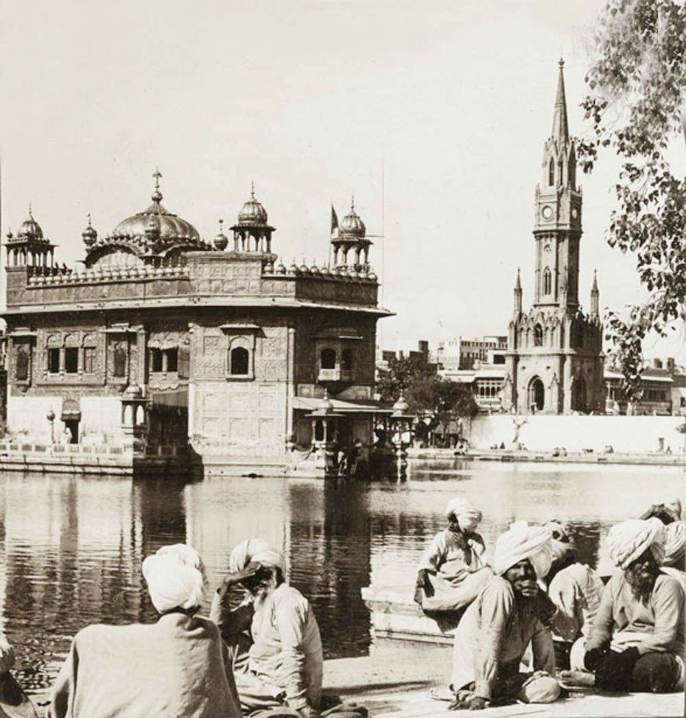 People sitting in pathway with Harmandir Sahib and Clock Tower in background
